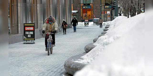 A cyclist bundled up against the cold rides by snowed tree tubs along W Madison St on Tuesday, Feb. 9, 2021, in Chicago. (AP Photo/Shafkat Anowar)