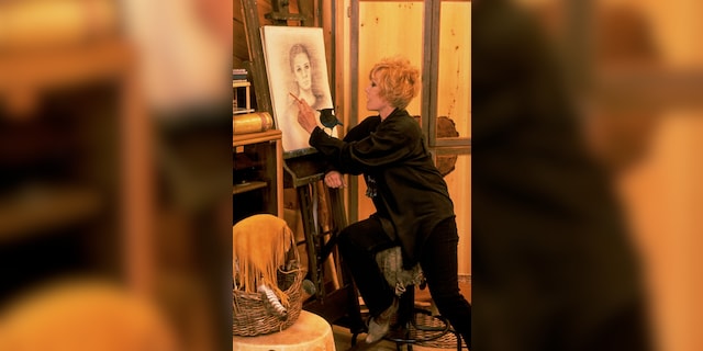 Retired actress Kim Novak sketching a portrait of an unidentified girl as a pet blue jay stands on her arm.