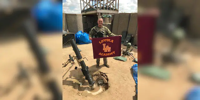 SPC George Kemper holds a Loyola Academy flag while serving in the U.S. Army.