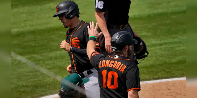San Francisco Giants' Wilmer Flores and Evan Longoria (10) score on a double hit by Curt Casali during the third inning of a spring training baseball game against the Oakland Athletics, Monday, March 29, 2021, in Mesa, Ariz. (AP Photo/Matt York)