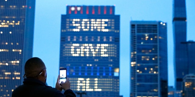 A person takes a photo, Sunday, May 30, 2021, of an illuminated sign on Chicago's Blue Cross Blue Shield Tower displaying "Some Gave All" in honor of Memorial Day. (AP Photo/Shafkat Anowar)