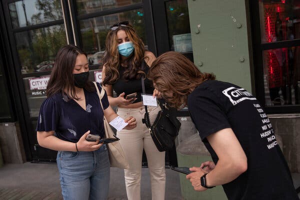Two patrons showed their vaccination cards to an employee before entering a venue in Manhattan in May. Local governments and private businesses are looking at mandates to increase vaccination rates.
