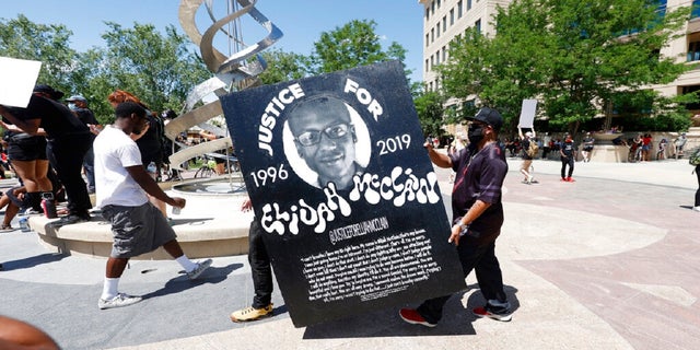 Demonstrators carry a giant placard during a rally and march over the death of Elijah McClain outside the police department in Aurora, Colorado, on June 27, 2020.