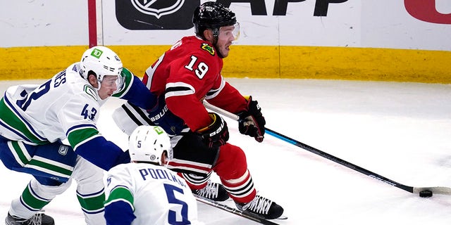 Chicago Blackhawks center Jonathan Toews (19) controls the puck against Vancouver Canucks defenseman Quinn Hughes (43) and defenseman Tucker Poolman during the second period of an NHL hockey game in Chicago, Thursday, Oct. 21, 2021.
