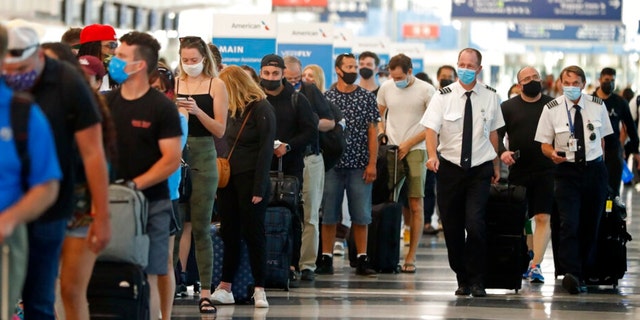 Two airplane pilots pass by a line of passengers while waiting at a security check-in line at O'Hare International Airport in Chicago, ahead of Fourth of July weekend, July 1, 2021. (AP Photo/Shafkat Anowar, File) 