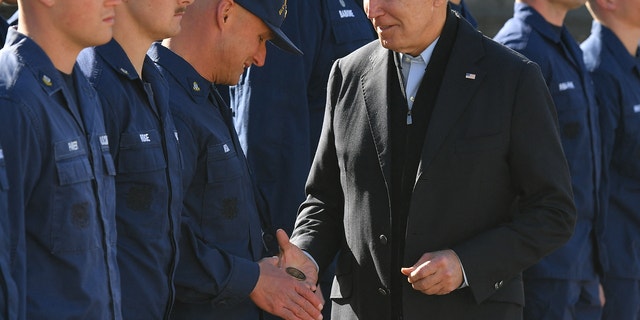 Biden hands a service member a challenge coin as he greets members of the Coast Guard at U.S. Coast Guard Station Brant Point in Nantucket, Mass., Nov. 25, 2021.  
