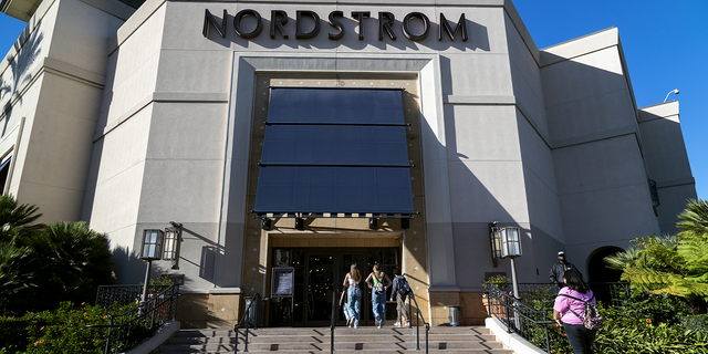 A security guard patrols the front entrance of Nordstrom on Nov. 23 as shoppers enter after an organized group of thieves attempted a smash-and-grab robbery at The Grove location in Los Angeles. An Allied Universal executive said the demand for additional security from clients has increased as organized thefts continue. 