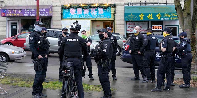 Seattle Police officers confer after taking part in a public roll call at Hing Hay Park in Seattle's Chinatown-International District Thursday, March 18, 2021.