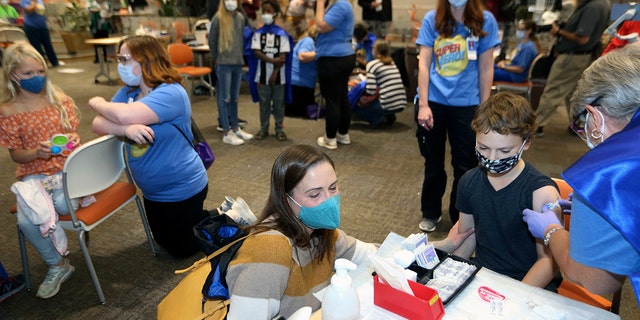 FILE - Retired registered nurse Jill Rill, right, puts a bandage on Jackson Stukus, 11, after he received a Pfizer COVID-19 vaccine as his mom Kristin looks on during the first COVID-19 vaccine clinic in Franklin County for children age 5-11 at Nationwide Children's Hospital in Columbus, Ohio, Nov. 3, 2021. (AP Photo/Paul Vernon, File)