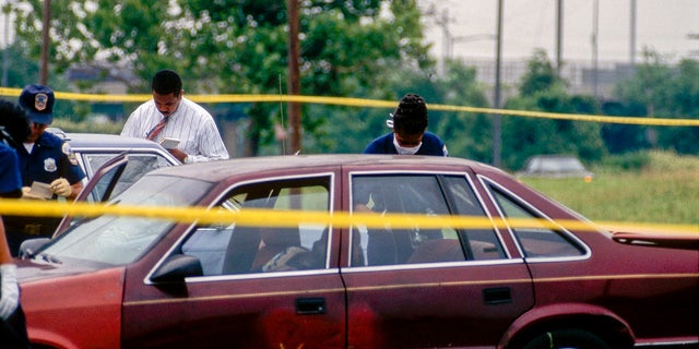 DC homicide detectives examine evidence in a car at a murder crime scene, Washington DC, 1996. The victim's body was found in the parked car. 