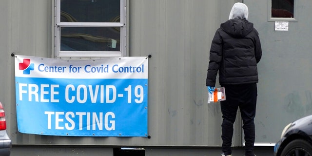 A sign about COVID-19 testing is displayed outside of COVID-19 testing site as a health walker collects testing tube in Wheeling, Ill., Friday, Dec. 3, 2021. A week after Thanksgiving, Illinois on Thursday reported this year's highest daily total of new coronavirus cases, while COVID-19 hospitalizations have risen higher than any point since last winter. (AP Photo/Nam Y. Huh) 