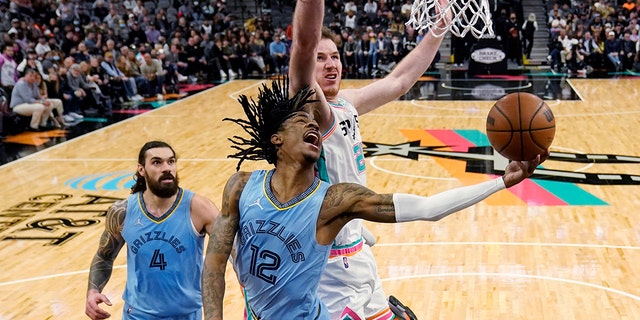 Memphis Grizzlies guard Ja Morant (12) drives to the basket against San Antonio Spurs center Jakob Poeltl (25) during the second half of an NBA basketball game, Wednesday, Jan. 26, 2022, in San Antonio.