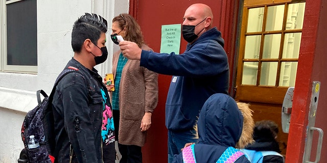 John Marro, the dean of students at P.S. 347, The American Sign Language and English Lower School, in New York, takes students' temperatures as they arrive on the first day after the holiday break, Monday, Jan. 3, 2022. 