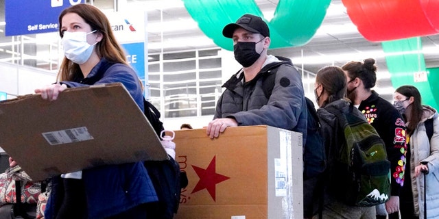 Travelers line up wearing protective masks indoors at O'Hare International Airport in Chicago, Tuesday, Dec. 28, 2021.  