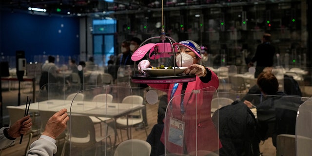 A worker grabs food delivered to a table robotically in the media dining area of the main media center ahead of the 2022 Winter Olympics, Wednesday, Feb. 2, 2022, in Beijing. 