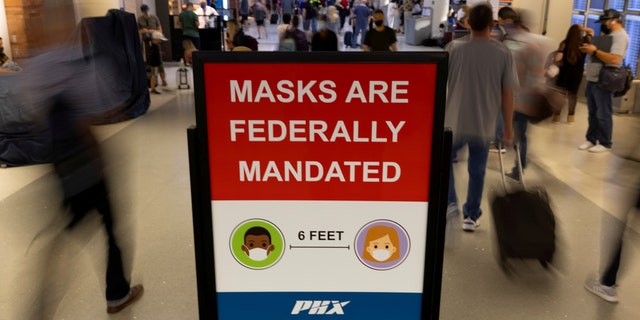 Air travelers make their way past a sign mandating face masks for all. REUTERS/Mike Blake