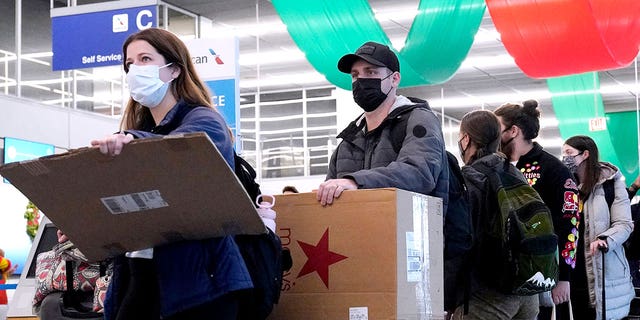 FILE - Travelers line up wearing protective masks indoors at O'Hare International Airport in Chicago, Dec. 28, 2021. (AP Photo/Nam Y. Huh, File)