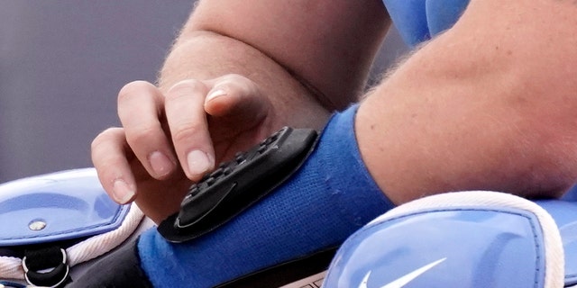 Kansas City Royals catcher Cam Gallagher uses a wrist-worn device used to call pitches during the sixth inning of a spring training game against the Seattle Mariners March 29, 2022, in Peoria, Ariz.