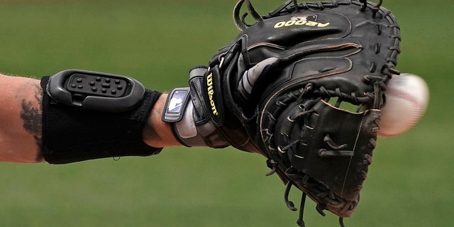 Seattle Mariners catcher Tom Murphy wears a wrist-worn device used to call pitches as he catches a ball during the sixth inning of a spring training game against the Kansas City Royals March 29, 2022, in Peoria, Ariz.