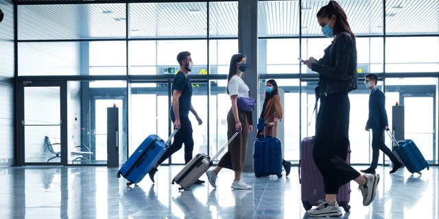 People traveling by plane during COVID 19, wearing N95 face masks, carrying luggage in airport terminal. (iStock)