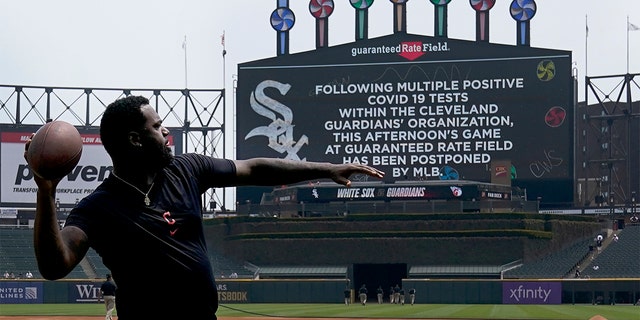 Cleveland Guardians' Franmil Reyes throws a football to teammate Myles Straw as the scoreboard informs fans that the baseball game between the Chicago White Sox and the Guardians has been postponed due to multiple positive COVID-19 tests within the Guardians organization, Wednesday, May 11, 2022, in Chicago.