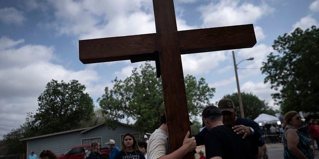 Dan Beazley and his son Joey Beazley, from Detroit, carry a wooden cross as they pray at a memorial outside Robb Elementary School in Uvalde, Texas, Monday, May 30, 2022.