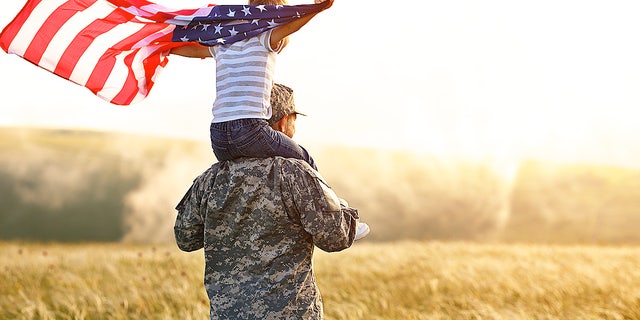 A child holds an American flag while sitting atop the shoulders of a military dad.