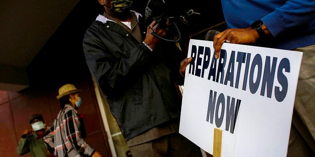 Vernon AME Church pastor Robert Turner holds a reparations now sign after leading a protest from City Hall
