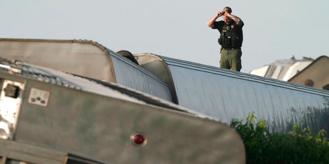 A law enforcement officer inspects the scene of an Amtrak train which derailed after striking a dump truck Monday, June 27, 2022, near Mendon, Mo. 