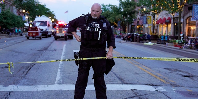 A police officer holds up police tape at the scene of a mass shooting at the Highland Park Fourth of July parade in downtown Highland Park, a Chicago suburb, on Monday, July 4, 2022.