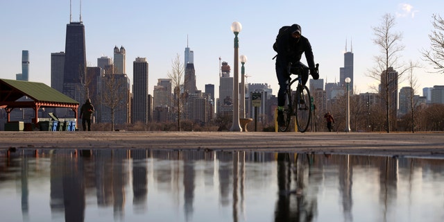 FILE - The Chicago skyline is reflected in the water of the thawed snow as a cyclist passes by at North Avenue Beach on March 1, 2021, in Chicago. (AP Photo/Shafkat Anowar, File)