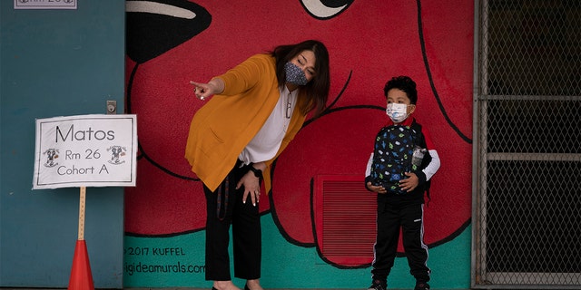 Kindergarten teacher Lilia Matos and her student Jesus Mendez stand outside their classroom on the first day of in-person learning at Heliotrope Avenue Elementary School in Maywood, Calif., April 13, 2021.  