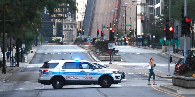 A pedestrian walks across Michigan Ave., Monday, Aug. 10, 2020, past a Chicago police department vehicle, a few blocks north of the raised Michigan Avenue bridge over the Chicago river.