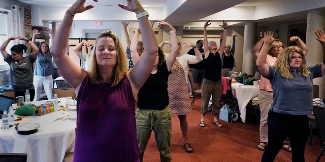 Instructor Emily Daniels, left, raises her arms while leading a workshop helping teachers find a balance in their curriculum while coping with stress and burnout in the classroom, Tuesday, Aug. 2, 2022, in Concord, N.H.
