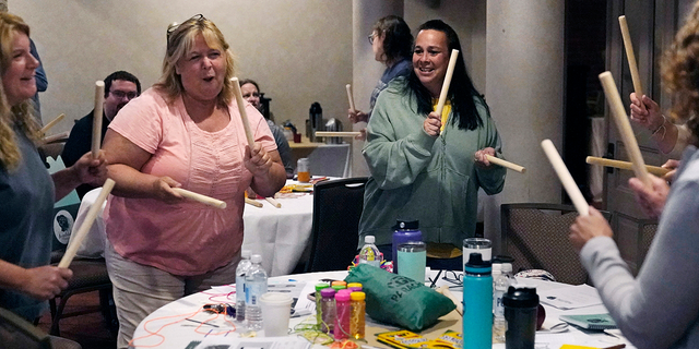 Teachers and guidance counselors tap wooden sticks during a rhythm exercise during a workshop helping teachers find a balance in their curriculum while coping with stress and burnout in the classroom, Tuesday, Aug. 2, 2022, in Concord, N.H.