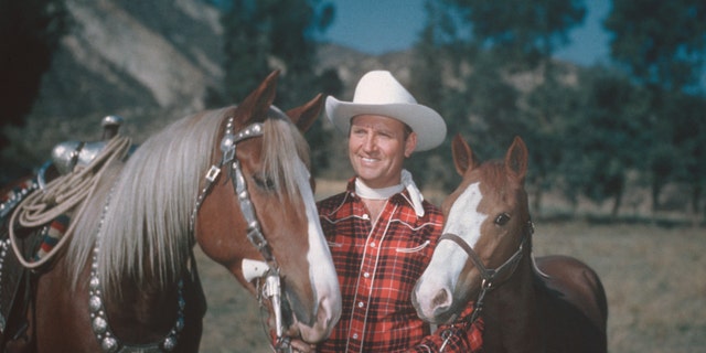 Country and western singer Gene Autry (1907-1998), dressed in cowboy hat and plaid shirt, poses with two horses, circa 1955. Autry gained fame as "The Singing Cowboy" on the radio, in movies and on television. 