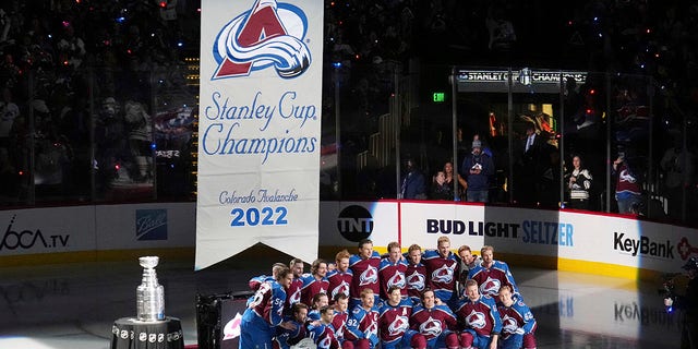 Members of the Colorado Avalanche pose with the championship banner before it was lifted into the arena on Wednesday, Oct. 12, 2022, in Denver.