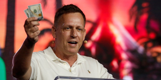 Peter Thiel, co-founder of PayPal, Palantir Technologies, and Founders Fund, holds hundred dollar bills as he speaks during the Bitcoin 2022 Conference at Miami Beach Convention Center on April 7, 2022, in Miami, Florida. 