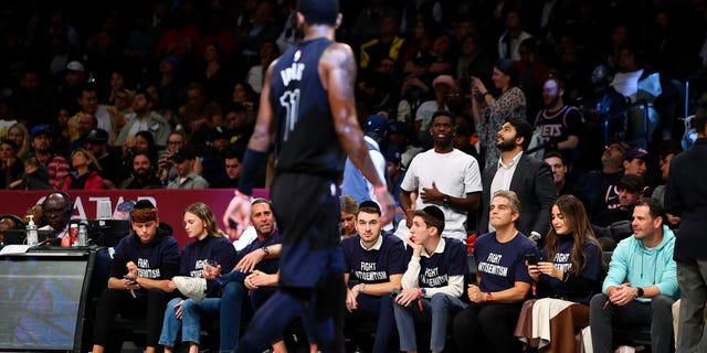 Fans with matching shirts look on as Brooklyn Nets guard Kyrie Irving, #11, walks by during the first half of an NBA basketball game against the Indiana Pacers, Monday, Oct. 31, 2022, in New York.