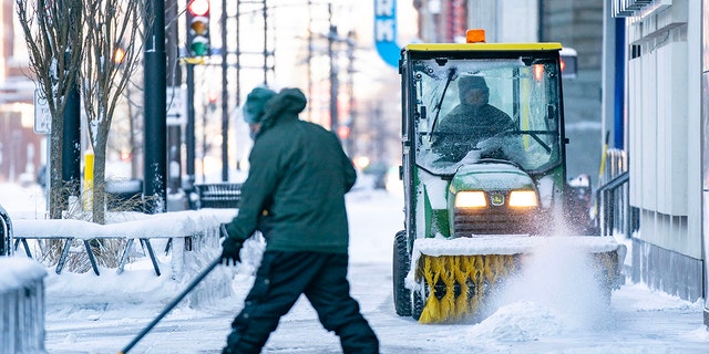 A man shovels the sidewalk while another one clears the snow with a power sweeper Thursday, Dec. 22, 2022 in downtown Minneapolis.