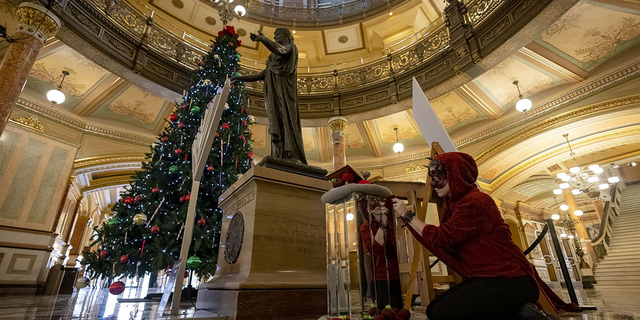 A person who goes by the name Laocoon polishes the mirrored base under the Satanic Temple of Illinois display on Dec. 6, 2022, at the Illinois State Capitol.