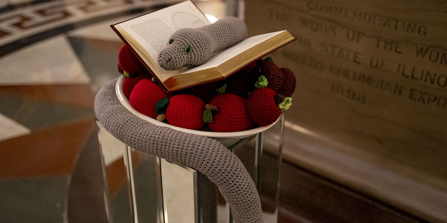 A crocheted snake and apples and a book by Copernicus on Dec. 6, 2022, make up the seasonal display placed by members of the Satanic Temple of Illinois at the Illinois State Capitol.