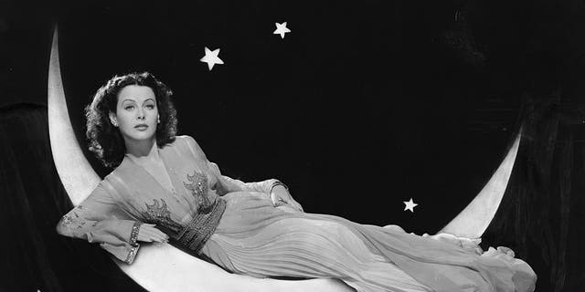 August 4, 1943: Austrian-born actress Hedy Lamarr (1913-2000) models a long flowing dress while reclining on a crescent moon in a publicity shot for her film "The Heavenly Body." 