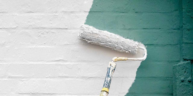 A paint roller covered in white paint coats a green wall.