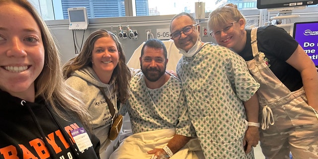 John Primavera (in glasses) stands next to good friend and kidney donor Tom Kenny (sitting in hospital bed), along with members of their families, after their successful transplant surgery at NYU Langone Health in New York. 