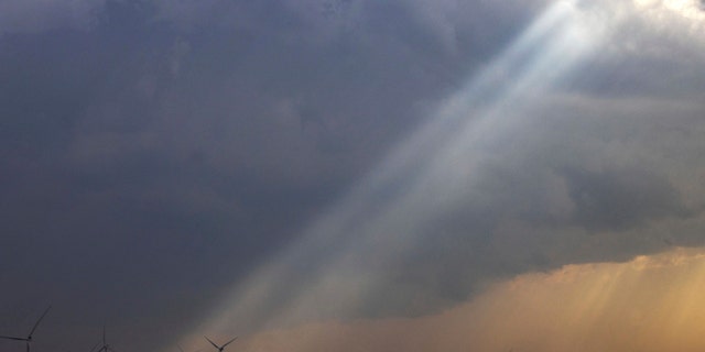 Sunlight filters through storm clouds onto a wind turbine as severe weather rolls through the Midwest on April 4, 2023, south of Stuart, Iowa.