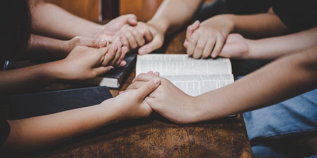 group holding hands praying with open Bible
