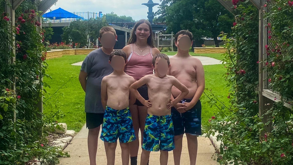 Teen girl poses with her four brothers outside.
