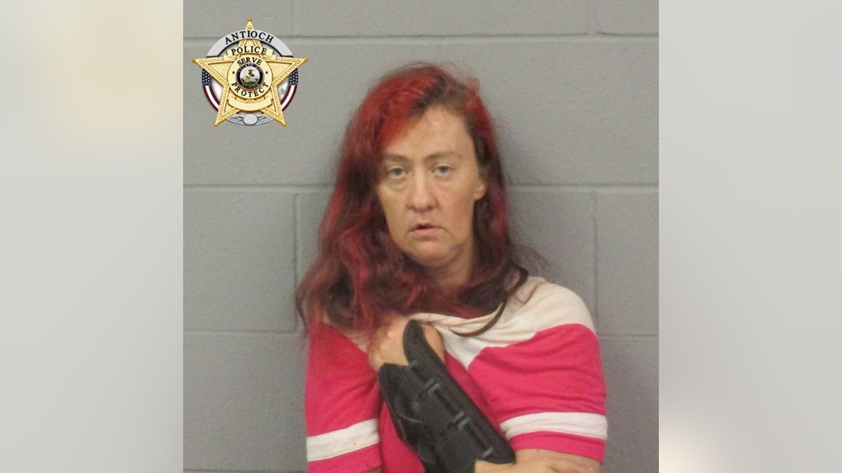 Julie Anderson, wearing an arm cast, is seen wearing a pink and white short for a police mugshot.