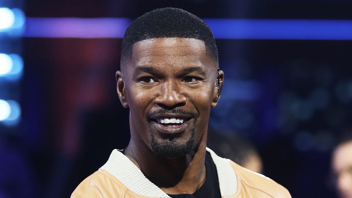 Jamie Foxx in a yellow jacket with white trim smiles on the set of "BEAT SHAZAM"